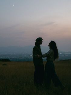 two people standing in a field with the sun setting behind them and one person holding his hand