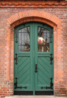 a green double door with two windows in front of a brick wall and an arched doorway