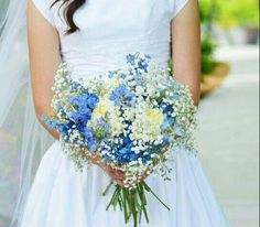 a woman in a white dress holding a bouquet of blue and white flowers on her wedding day