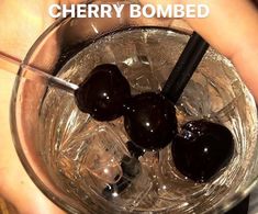 there is a person holding a glass with two cherries in it and the words cherry bomb