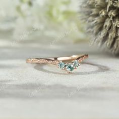 a rose gold ring with three green stones on the side and a pine cone in the background