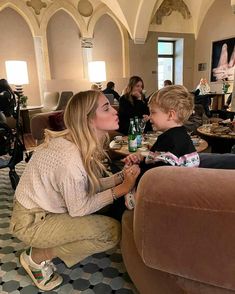 a woman sitting on the floor next to a little boy in a room filled with people