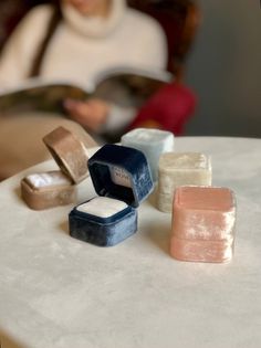 three different colored soaps sitting on top of a table next to a woman in a white sweater