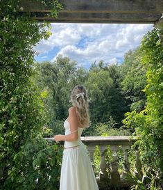 a woman in a white wedding dress looking out at the trees and bushes around her