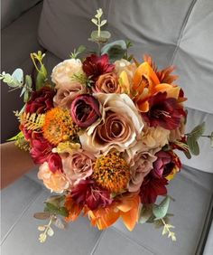 a bridal bouquet with orange, red and yellow flowers on a couch in a living room