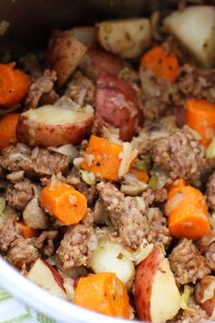 a pot filled with meat, potatoes and carrots on top of a green towel