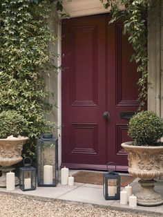 a red door surrounded by potted plants next to two urns with candles on them