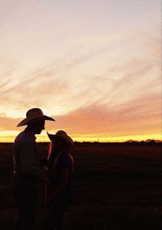 two people standing next to each other in a field with the sun setting behind them