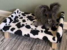 a cat sitting on top of a cow print dog bed in the corner of a room