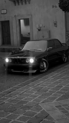 a black and white photo of a car parked in front of a building with its lights on