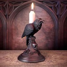 a black bird sitting on top of a wooden table next to a white lit candle