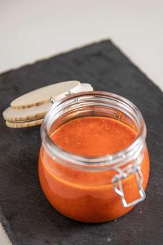 an orange sauce in a glass jar with a wooden spoon next to it on a slate board