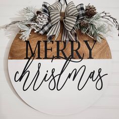 a merry christmas sign hanging on the side of a wall with pine cones and evergreens