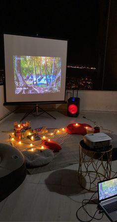 a projection screen on the roof of a building with candles in front of it and laptops nearby