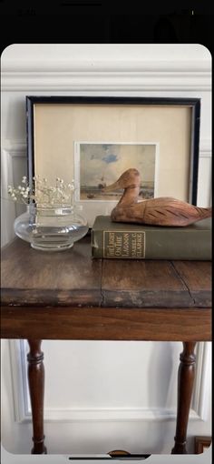 a bird statue sitting on top of a wooden table next to a book and vase