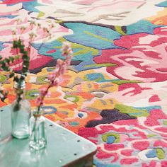 two vases filled with flowers sitting on top of a table next to a rug