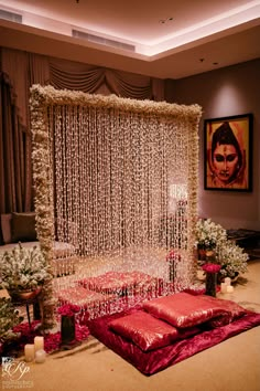 a decorated stage with red pillows and white garlands on the wall, surrounded by greenery