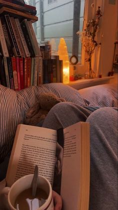 a person laying in bed reading a book and holding a coffee mug with a spoon sticking out of it