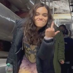 a woman giving the peace sign while standing in front of a metal pipe and other people