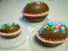 three chocolate covered desserts sitting on top of two clear plates with pink, blue and green decorations