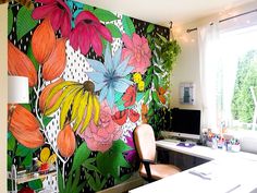 an office decorated with colorful flowers and plants on the wall, next to a computer desk