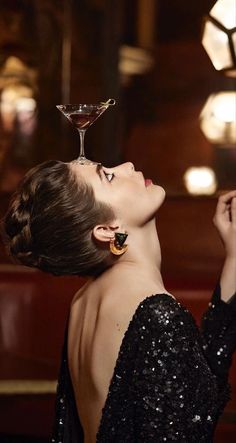 a woman in a black dress holding a martini glass up to her face