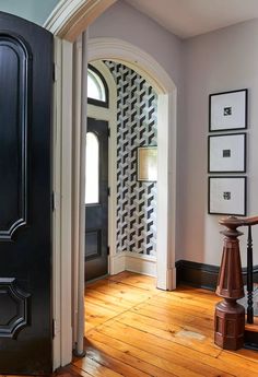 an entry way with a wooden floor and black door, framed pictures on the wall