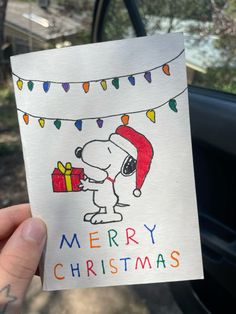 a hand holding up a christmas card with a cartoon character on it and a string of lights