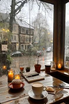 a cup of coffee sitting on top of a wooden table next to a window covered in rain