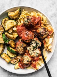 a white plate topped with meatballs and veggies next to a fork on a marble table