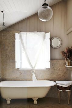 an old fashioned bathtub in the corner of a bathroom with white curtains and windows