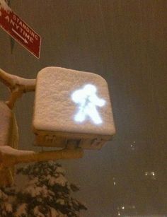 a snow covered street sign with a person walking on it's backlited in the snow