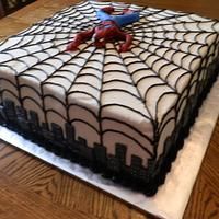 a spider - man cake on a wooden table with white frosting and black icing