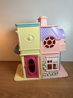 a small toy house on a table with the door open and windows painted pink, blue, yellow and green