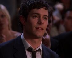 a man in a suit and tie looking at the camera while people look on from behind him