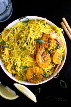 a bowl filled with noodles and shrimp next to lemon wedges on a black surface