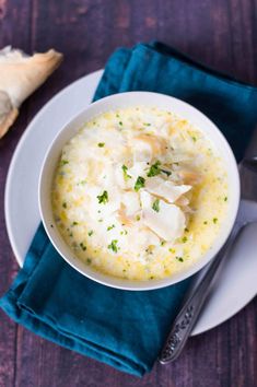 a white bowl filled with soup on top of a blue napkin next to a spoon