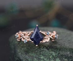 a blue diamond ring sitting on top of a green rock with leaves and stones around it