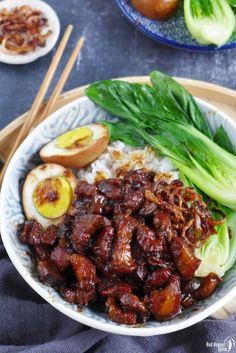 a bowl filled with meat and vegetables next to chopsticks on a table top