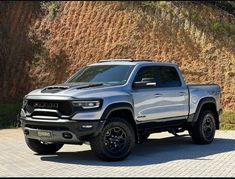 a silver truck is parked in front of a mountain side wall with black rims