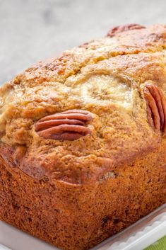 a loaf of bread with pecans on top in a white container next to a green napkin