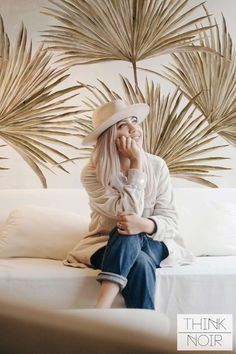 a woman sitting on top of a white couch in front of palm tree wallpaper