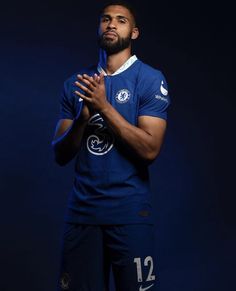 a man in a blue soccer uniform is holding his hands together while standing against a dark background