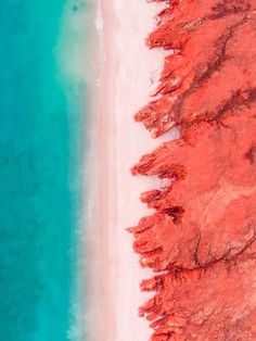 an aerial view of the beach and ocean with red sand, blue water and white sand