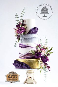 a three tiered cake with purple flowers and greenery on top, next to an acd seal