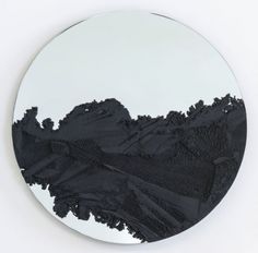 a round mirror with black paint on the surface and mountains in the backround