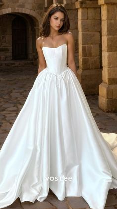 a woman in a white wedding dress standing on a stone floor with her hands behind her back