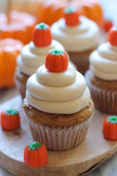 several cupcakes with white frosting and orange pumpkin decorations on a wooden board