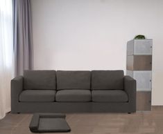 a grey couch sitting next to a window in a living room on top of a hard wood floor