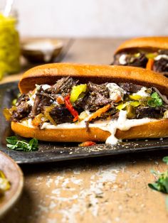 two sandwiches with meat, cheese and vegetables on a black platter next to other food items